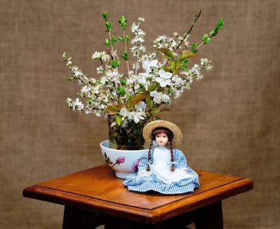 Charming Porcelain Doll in Gingham Dress with Spring Cherry Blossoms on Wooden Table image