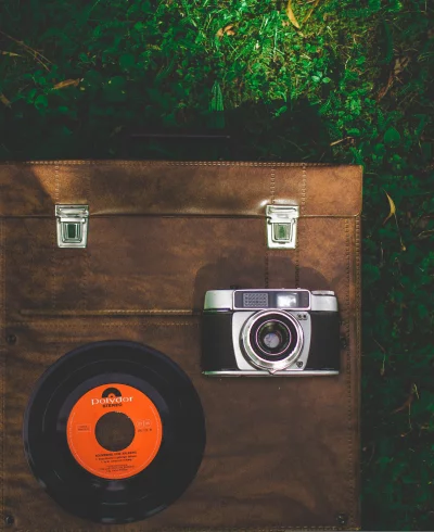 A flat lay of a vintage camera and a vinyl record on a brown leather case
