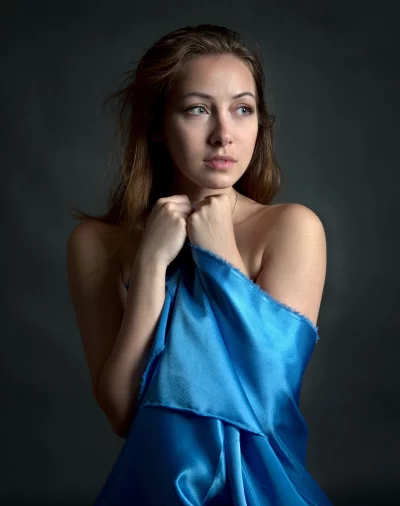 Pensive Young Woman Draped in Blue Satin Fabric with Expressive Gaze image