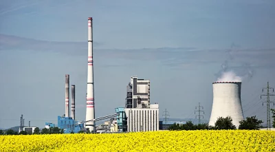 Industrial Power Plant with Cooling Tower and Smokestacks Overlooking a Vibrant Rapeseed Field image
