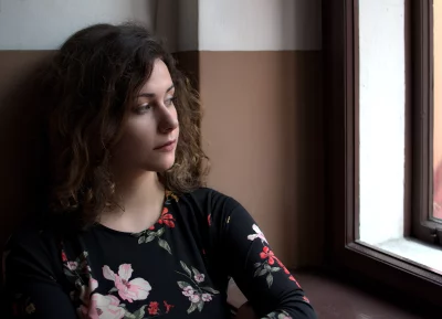 Pensive Young Woman with Curly Hair Gazing Out Window in Floral Top image