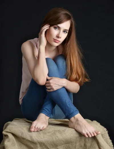 Pensive Young Woman Sitting in Jeans and Pink Top on Burlap image