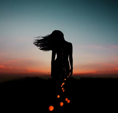Ethereal Silhouette of Woman with Glowing Orbs Against Sunset Sky image