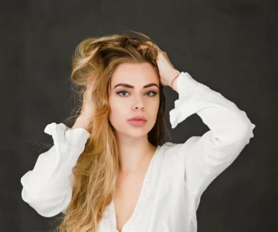 Blonde Woman with Wavy Hair and Hands in Hair Posing on Dark Background image