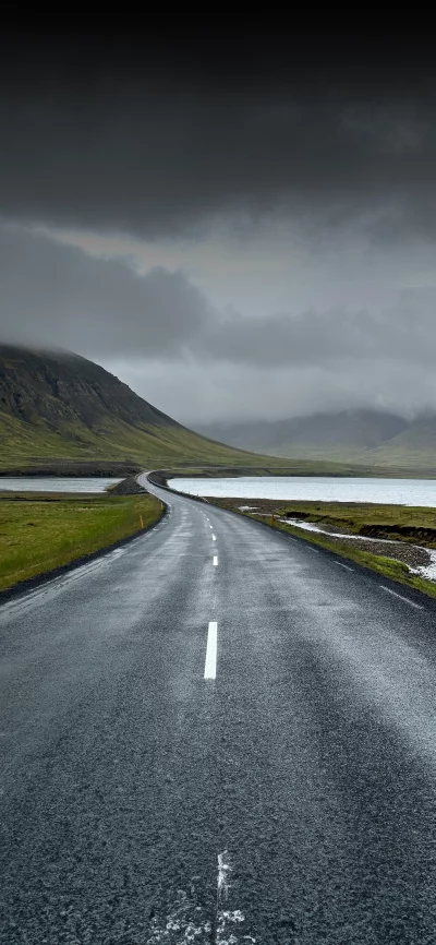Empty scenic asphalt road winding through a dramatic Icelandic landscape under moody skies
