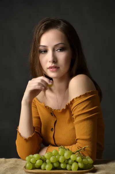 Elegant Young Woman with Pensive Gaze and Green Grapes image