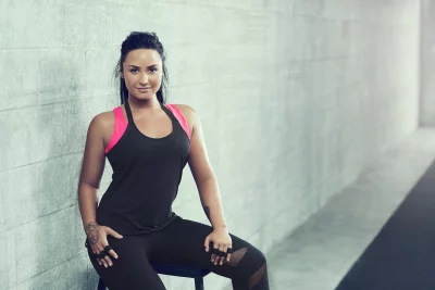 Strong Woman in Black and Pink Sportswear Sitting Confidently Against Textured Concrete Wall image
