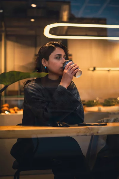 Young Woman Savoring Hot Coffee in a Cozy Cafe Evening Scene