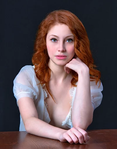 Pensive Redhead Woman with Freckles in Sheer Top at Wooden Table image