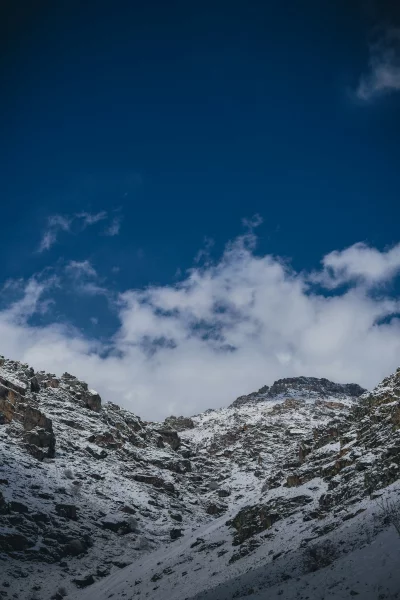 Snow-covered rocky mountains under a vast blue sky with clouds