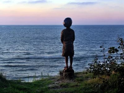 Young Child in Helmet Contemplating Vast Ocean Horizon at Tranquil Sunset image