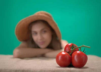 Vibrant Red Tomatoes with Water Drops and Blurred Woman in Hat Against Green Backdrop image