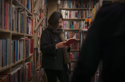 Young woman reading a book in a bookstore aisle filled with shelves of books