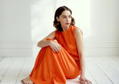 Elegant Woman in Vibrant Orange Dress Sitting on Rustic White Floor Looking Thoughtfully image