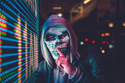 Anonymous Hacker in Skull Mask with Silent Gesture Against Vibrant LED Data Display image