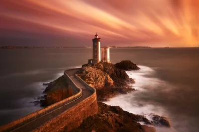 Dramatic Long Exposure Sunset over Iconic Lighthouse on Rocky Coastal Path image