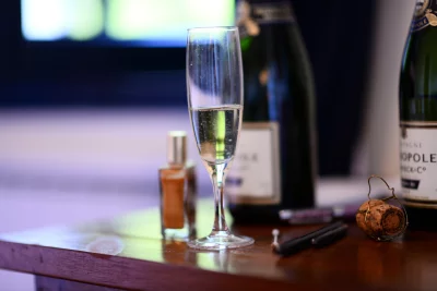a still life of a champagne glass, a bottle of champagne, a cork, a lighter and what seems like a perfume bottle