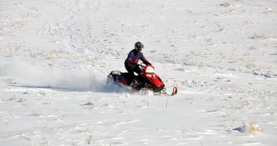 Adventurous Snowmobile Rider Navigating Winter Snow Field with Dry Grass image