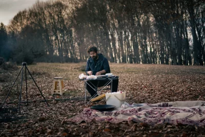 Man Preparing Food at a Rustic Outdoor Campsite in Autumn Woods