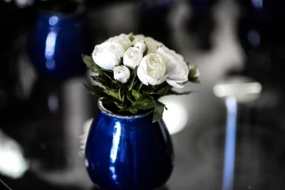 A beautiful still life of a blue vase with white flowers sitting on a black table