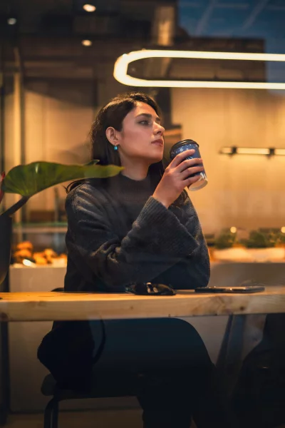 Thoughtful Woman Enjoying Coffee in a Cozy Cafe Setting with Ambient Light