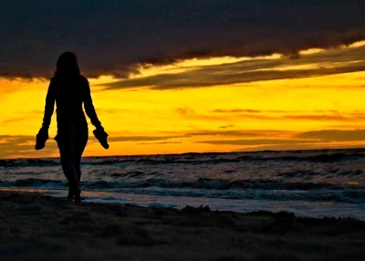 Woman's Silhouette Walking on Tranquil Beach at Golden Sunset Hour image