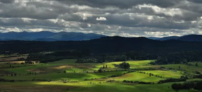 Dramatic Sunbeams Illuminate Verdant Fields and Layered Mountains Under an Overcast Sky image