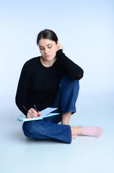 Focused Young Woman Writing in Blue Notebook on White Background image