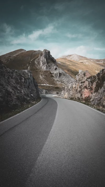 Winding Mountain Road Through Rocky Landscape Under Cloudy Sky