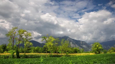 Dramatic Cloudy Mountain Landscape with Lush Green Fields and Trees image