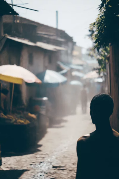 Silhouette of a man walking through a dusty market street with stalls and umbrellas