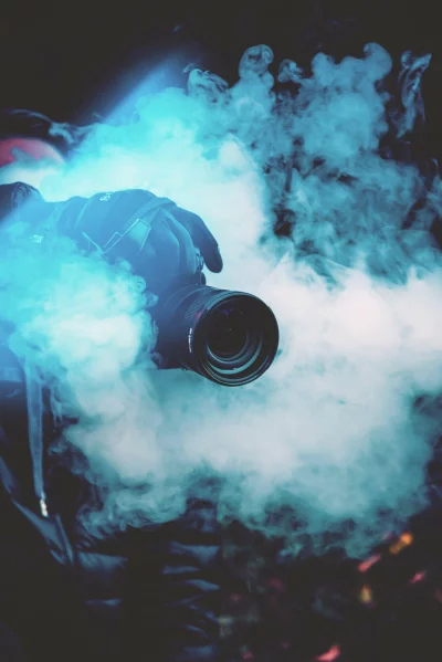 Photographer's Gloved Hand Holding Camera Amidst Vibrant Blue Smoke and Mysterious Lighting image