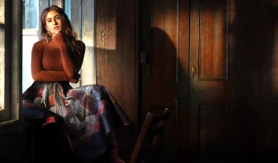 Captivating Young Woman by Window with Dramatic Light and Elegant Patterned Skirt image