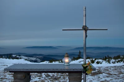 Glowing Candle by Metal Cross on Snowy Mountain Peak at Twilight image