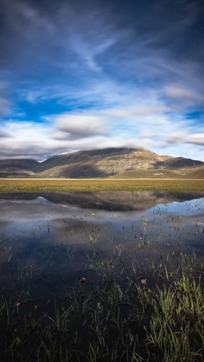 Dramatic mountain landscape reflected in calm lake under wispy clouds