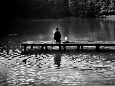 Lone Figure Kneeling on Wooden Pier by Serene Lake in Monochrome Morning image