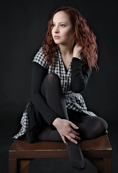 Redhead Woman in Plaid Shirt Sitting Thoughtfully on Dark Background image