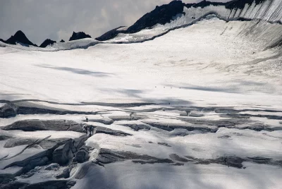 Mountaineers traversing a vast glacier with deep crevasses under dramatic cloudy skies image