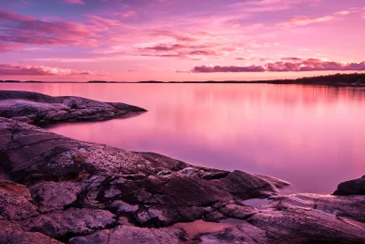 Vibrant Pink and Purple Sunset Sky Reflecting on Calm Lake with Rocky Shore image