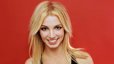 Smiling Blonde Pop Icon Britney Spears Posing Confidently on Vibrant Red Background image
