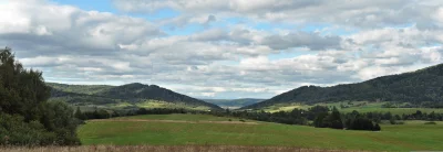 Panoramic Green Valley with Forested Mountains, Lush Fields, and Cloudy Sky image