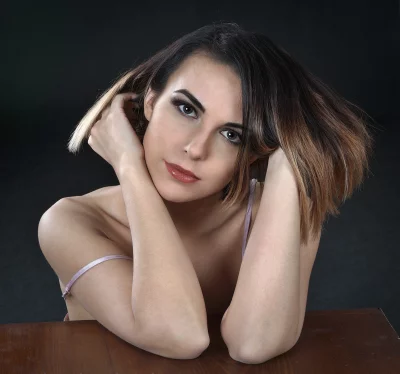 Elegant Young Woman with Expressive Gaze, Resting Her Elbows Gracefully on a Wooden Table image