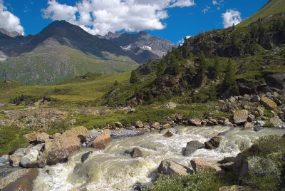 Mountain River Rushing Through a Green Alpine Valley with Majestic Peaks image