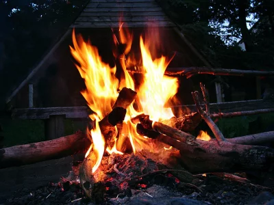 Bright Campfire Burning with Vivid Flames Against Dark Rustic Cabin at Dusk image