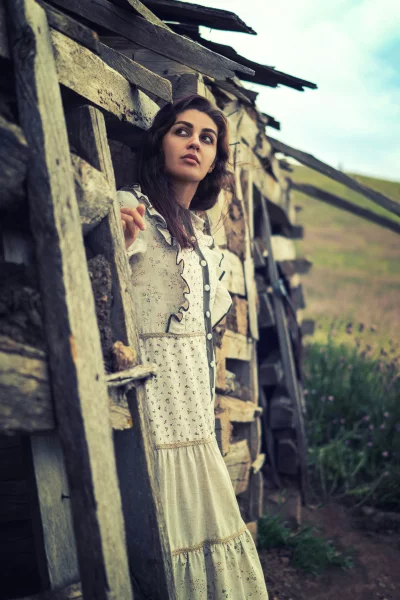 Pensive Woman in Vintage Floral Dress by Weathered Wood Structure