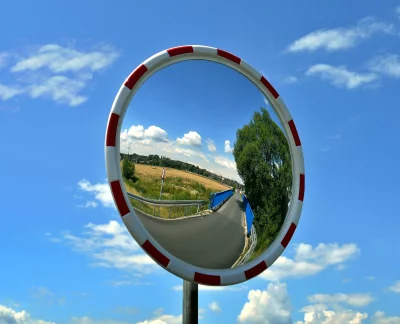 Round Traffic Mirror Reflecting a Serene Rural Road and Blue Sky image