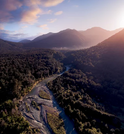 Majestic River Flowing Through Lush Forest and Mountains at Golden Hour image