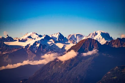 Panoramic Alpine Landscape at Golden Hour: Snow-Capped Mountains, Forest, and Clear Blue Sky image