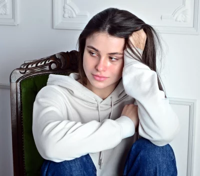 Thoughtful Young Woman in White Hoodie Sitting on Vintage Green Chair Contemplating Life image