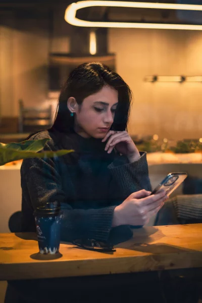 Woman using phone sitting at wooden table indoors